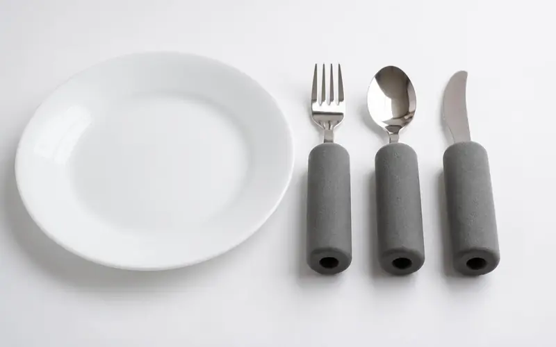 Illustration of a fork, spoon and knife with thick foam handles beside a plate.