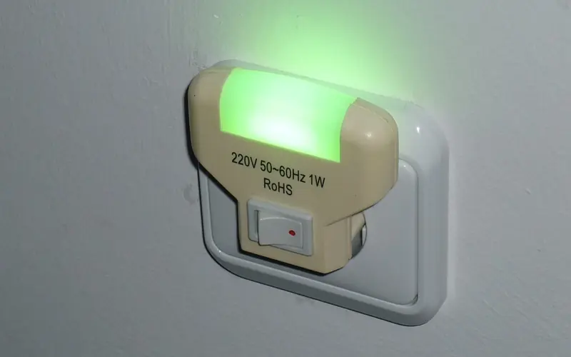 Photo of a plug-in LED night light glowing green in a wall socket.