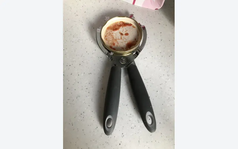 Photo of a hand-held jar opener with black rubber grips on a jar lid. Shows the type of product, not the exact brand or model.