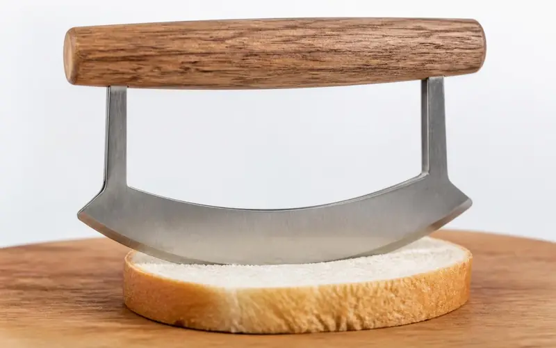 Illustration of a rocker knife with a curved blade and wooden handle cutting bread.