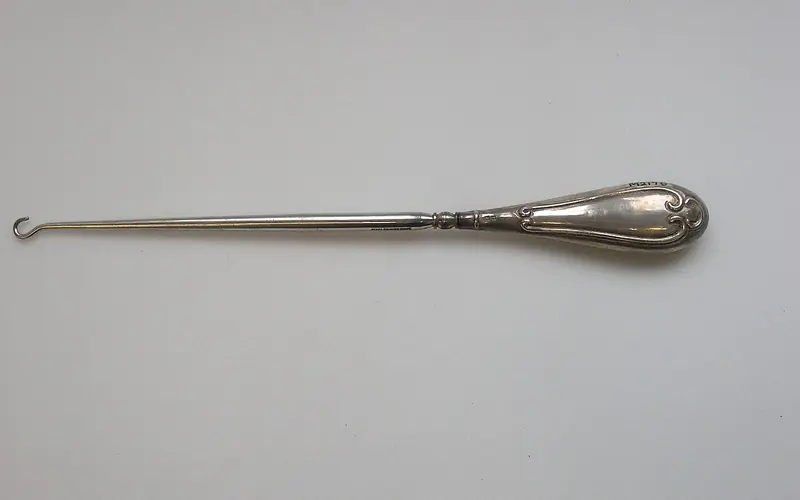 Photo of a metal button hook with a decorated handle.
