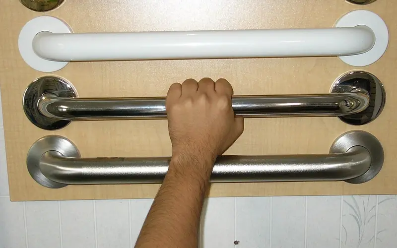 Photo of a hand gripping a stainless steel grab bar mounted on a wall.