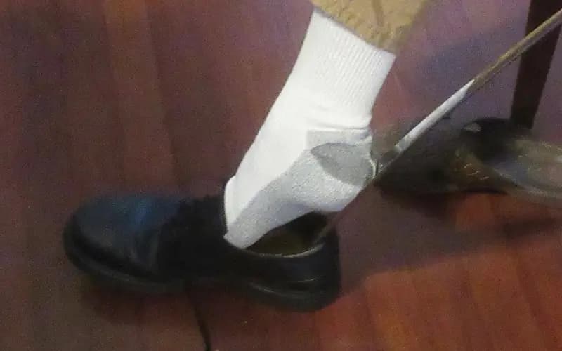 Photo of a person sliding a foot into a shoe using a long metal shoe horn.