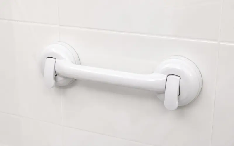 Illustration of a white suction-cup grab handle attached to bathroom tiles.