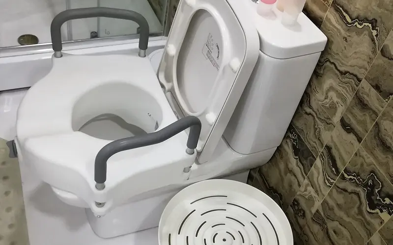 Photo of a raised toilet seat with grey armrests fitted on a toilet.
