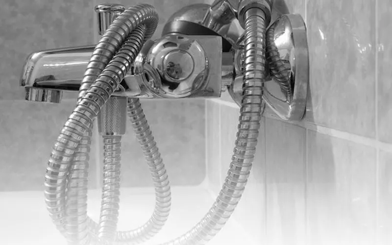 Photo of a chrome handheld shower head and metal hose by a bath tap. Shows the type of product, not the exact brand or model.
